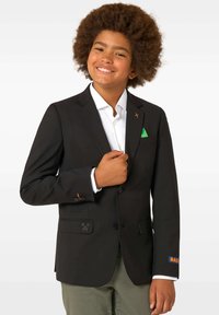 Melnā žakete ar vienu pogu, ar kabatām un dekoratīvām oranžām akcentiem. Baltā krekla ar apkakli, zem kura ir zaļš kabatlakats.