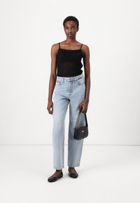 Musthave mustriba tank top, heledad sinine sirge säärega teksad, mustad lamekingad ja väike must kott logodetailiga. Neutraalne taust.