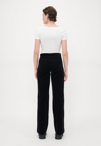 Black corduroy wide-leg trousers with a high waist, featuring a clean design and subtle stitching. Paired with a fitted white top.