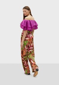 Blus med off-the-shoulder design i levende lilla flæser og bukser med vidde i blomsterprint, prydet med grønne, orange og pink blade.