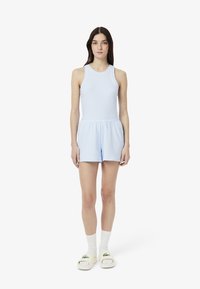 Conjunto de top atlético de tirantes en color azul claro y pantalones cortos con textura suave, que presenta un ribete blanco. Combinado con calcetas blancas hasta la rodilla y sandalias claras.