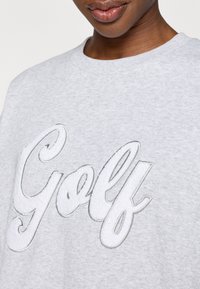 Sweatshirt cinza com um grande "Golf" bordado em branco com contorno cinza, gola redonda e textura suave.