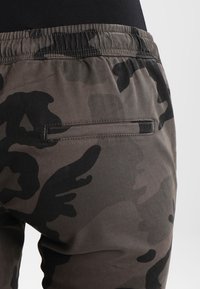 Kamouflage-mönstrade joggingbyxor i nyanser av grått och svart, med en stretchmidja och en bakficka med horisontell öppning.