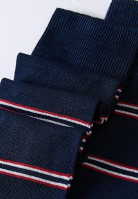 Marineblå sokker med ribbet tekstur, prydet med tre vandrette striber i hvid og rød. Stoffet ser blødt og elastisk ud, med et fladstrikket design.