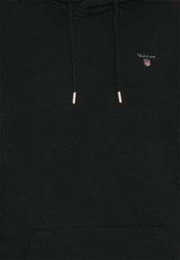 Zwarte hoodie gemaakt van zachte stof, voorzien van een voorzak, aantrekkoorden met zilverkleurige aglets en een klein geborduurd logo op de borst.