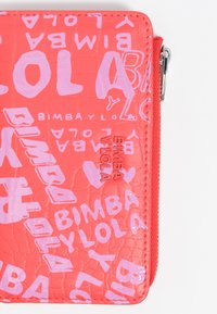 Czerwona portmonetka o teksturowanej powierzchni, ozdobiona różowymi abstrakcyjnymi literami oraz nazwą marki "Bimba Y Lola" wytłoczoną na metalowej płytce obok zamka.