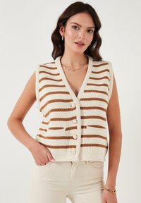 Gebreide mouwloze vest in crèmekleurige en bruine strepen, met een diepe V-hals, grote parelwitte knopen en vo pockets. Zachte textuur.