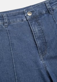 Donkerblauwe spijkerbroeken hebben een rechte snit, voorzakken, een knoopsluiting en zichtbare stiksels langs de naden.