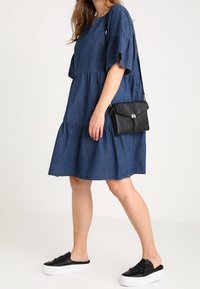 Jeansowa sukienka z krótkimi rękawami i warstwowym krojem, zestawiona z czarną torbą na ramię i czarnymi butami wsuwanymi z kokardą.