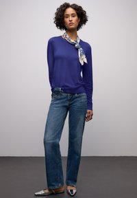 Pull à manches longues violet, jean bleu et ballerines argentées. Une écharpe à motifs orne le cou, et des lignes horizontales marquent la texture du pull.