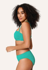 Tyrkysový bikini set s textúrovanou látkou. Vrchná časť má pevnú, podpůrnú konštrukciu, zatiaľ čo spodná časť má klasický strih.
