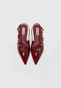Talons en cuir verni bordeaux à talon lâche avec des pointes aiguës, présentant plusieurs bandes et des accents de boucles dorées.