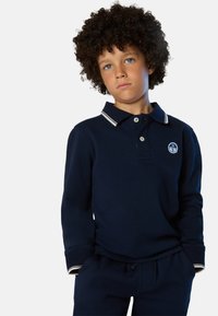 Polo a maniche lunghe blu navy con colletto e polsini bianchi, dotato di due bottoni e un piccolo logo sul petto, abbinato a pantaloni blu navy.