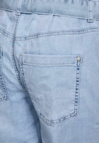 Pantalones cortos de mezclilla azul claro que presentan un bolsillo trasero con un acento de botón. La tela tiene un acabado suave y texturizado con costuras visibles.