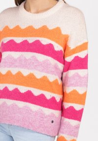 Sweter dziewiarski z zygzakowymi paskami w kolorze różowym, pomarańczowym i kremowym. Okrągły dekolt i teksturowane wykończenie. Mały detal z logo na końcu. 