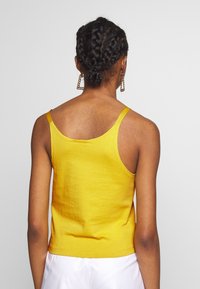 Gul ärmlös linne i mjuk bomull, med rundad rygg och smala spännen. Slät textur med en åtsittande silhuett.