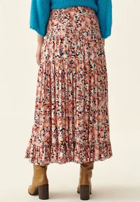 Floral maxi skirt in shades of pink, blue, and orange with a smocked waistband, tiered design, and ruffled hem. Paired with brown heeled boots.
