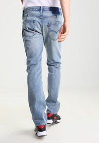 Light blue denim jeans with a straight fit, featuring back pockets and subtle faded detailing. Paired with black and red sneakers.