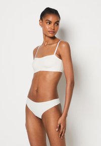 Bralette bianco senza cuciture e bikini abbinato, realizzati in un tessuto liscio. Il bralette presenta spalline sottili regolabili e un scollo dritto.