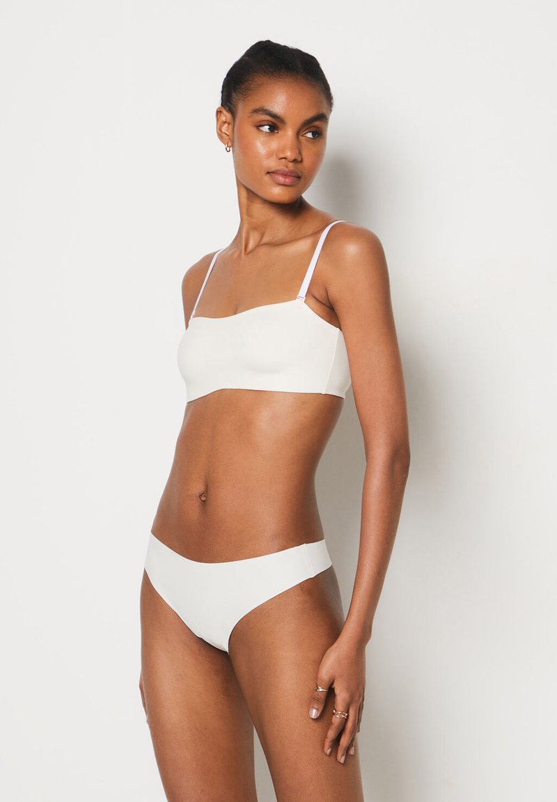 Bralette bianco senza cuciture e bikini abbinato, realizzati in un tessuto liscio. Il bralette presenta spalline sottili regolabili e un scollo dritto.