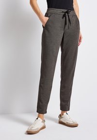Pantalons de jogging gris en tissu doux, avec des poches latérales, une taille élastique à cordon de serrage et des jambes fuselées. Assortis à des baskets blanches et beiges.