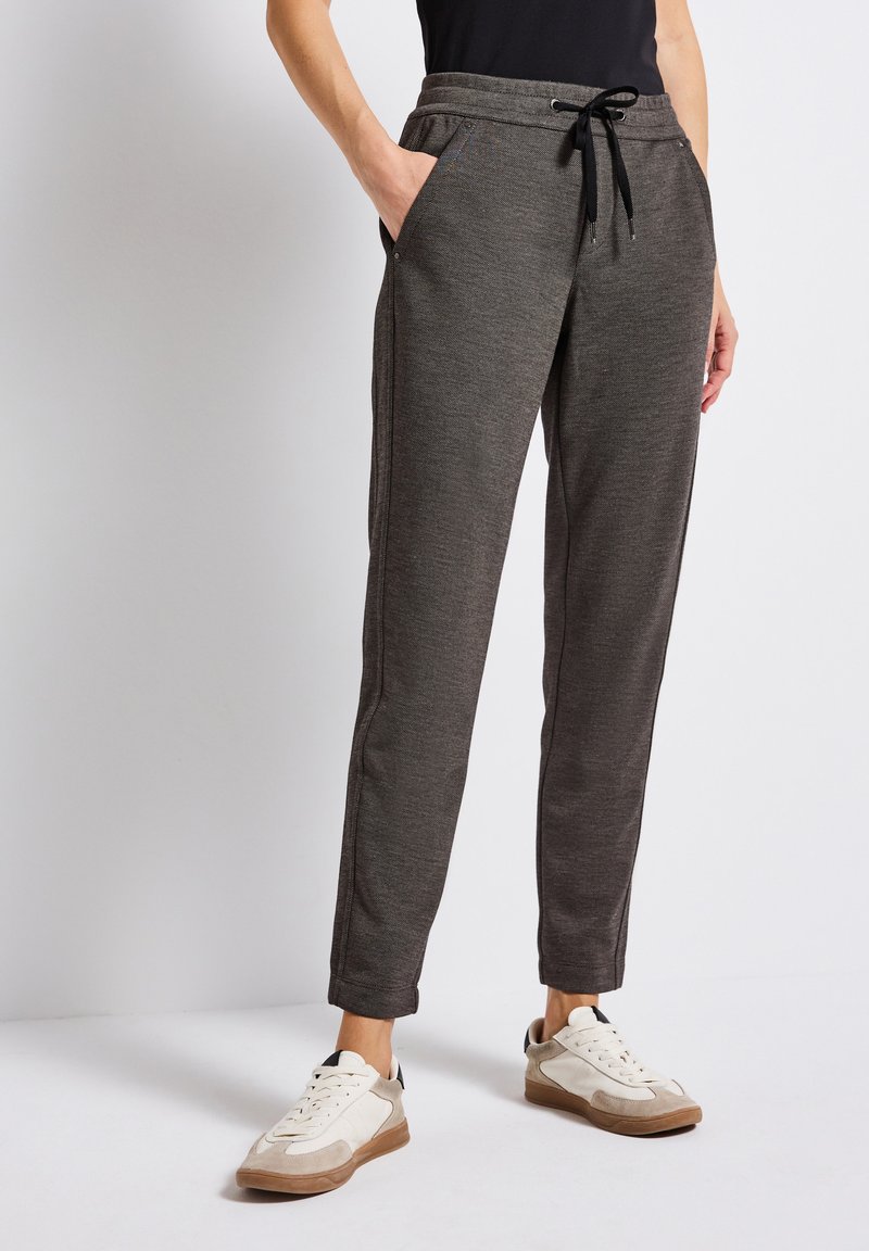 Pantalons de jogging gris en tissu doux, avec des poches latérales, une taille élastique à cordon de serrage et des jambes fuselées. Assortis à des baskets blanches et beiges.