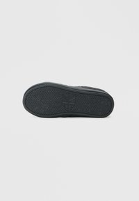 Suela de zapatilla negra con goma texturizada para agarre, que presenta un logo y un diseño estampado. Bordes suaves y curvas sutiles están presentes.