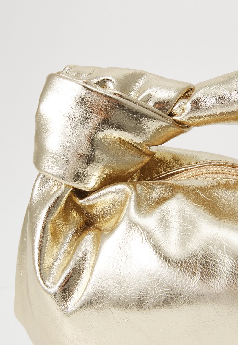 Bolso metálico dorado con un asa anudada, textura suave y arrugada, y cierre de cremallera. Presenta una superficie brillante y reflectante.