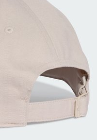Beige baseball cap with a textured fabric, curved visor, and adjustable strap featuring a metal clasp. Stitched detailing visible.