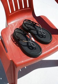 Sandales noires Havaianas à fines lanières reposant sur une chaise en plastique rouge sous un soleil éclatant.