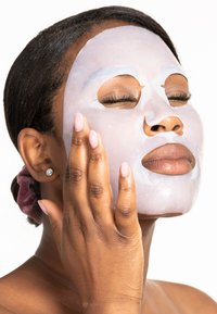Transparent sheetmask applicerad på ansiktet, slät textur, ljuslila nyans, modellens hand som rör vid sidan av ansiktet, naturliga naglar, kort hår.