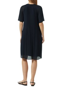 Navy-blaues, plissiertes Kleid mit kurzen Ärmeln, runder Halslinie und fließender Textur, das bis zur Mitte der Wade reicht, kombiniert mit flachen Sandalen.