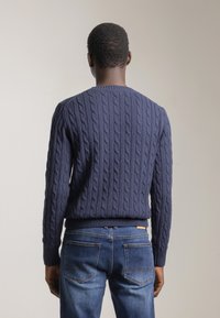 Jersey de punto en azul marino con cuello redondo, puños y dobladillo acanalados, combinado con jeans de denim de lavado medio que presentan un parche de cuero con el logo.