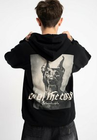 Czarna bluza z kapturem z dużym nadrukiem wizerunku wściekłego psa na plecach, z tekstem "Wydostany z klatki" i "Niezniszczalny."