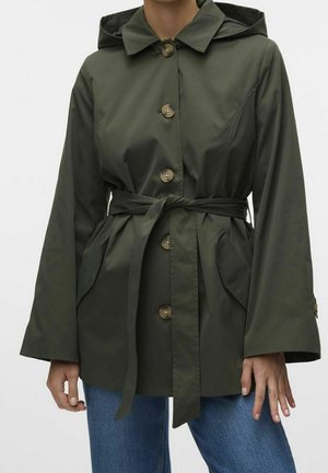 Oliivinvihreä hupullinen takki, jossa isot napit, solmittava vyötärövyö, etutaskut, päällä siniset farkut, kädet rentoina sivuilla.