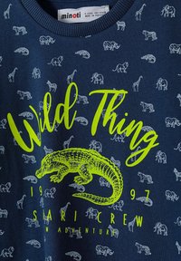 Camisa infantil de color azul marino con estampado repetido de animales grises y un gran texto en amarillo-verde que dice "Wild Thing" sobre una ilustración de cocodrilo en amarillo-verde.