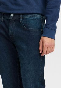 Mörkblå denimjeans med en slät yta, med klassisk femficksdesign och kontrasterande sömmar, parat med en blå, strukturerad långärmad skjorta.