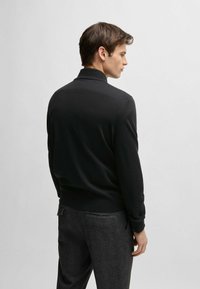 Black long-sleeve polo made of smooth fabric, featuring a turned-down collar and ribbed cuffs, paired with dark grey textured trousers.
