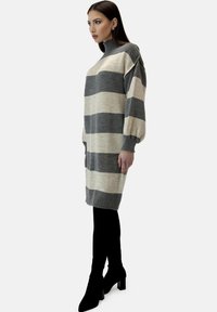 Strikket sweaterkjole med grå og cremefarvede striber, høj hals, løs pasform og ballonærmer, stylet med sorte knæhøje støvler.