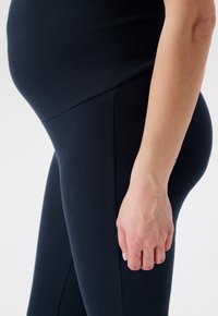 Zwarte geribbelde leggings met een hoge tailleband en zijnaad, die een zwangere silhoutte omarmen met een soepele textuur en een aansluitend ontwerp.