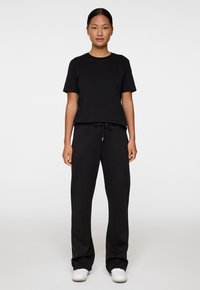 Musta puuvillapaita lyhyillä hihoilla, yhdistettynä mustiin verkkohousuihin, joissa on joustava vyötärö ja naru. Mallilla on päällään valkoiset tennarit.