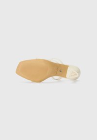 Beige high-heel sandal with a textured base, clear straps, and a logo accent. The sole is smooth with ribbed design for grip.
