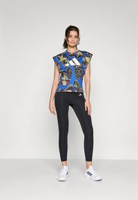 Blauwe top met vlinderprint, korte mouwen en een ronde hals, gecombineerd met zwarte legging en witte sportschoenen.