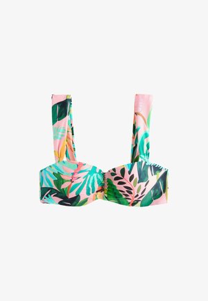 Close-up van een persoon die een badpak met bloemenprint draagt met groene, gele en oranje tropische patronen op een lichtroze achtergrond.