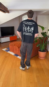 T-shirt preta de algodão com gráficos de basquetebol impressos a branco e texto nas costas, combinada com calças escuras e ténis prateados.