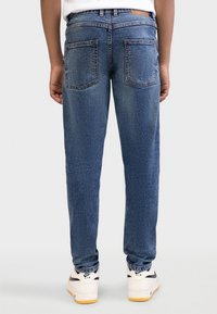 Μπλε τζιν παντελόνι με κανονική γραμμή, δύο τσέπες πίσω και κανονική μέση. Συνδυασμένο με λευκά αθλητικά παπούτσια Nike με μαύρες λεπτομέρειες.