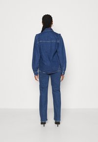 Jeansjacka och byxor i mörkblått, med lång ärm, krage och rak benform. Inkluderar knäppta ärmslut.