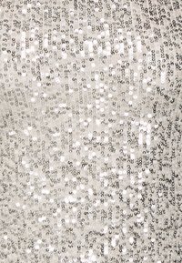 Sparkly silver top covered in small sequins, with a smooth texture and a fitted design, reflecting light in various directions.