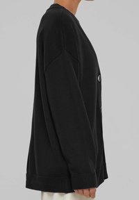 Cárdigan negro hecho de material de punto, con borde y puños de canalé, ajuste relajado y detalle de botones en el lateral.