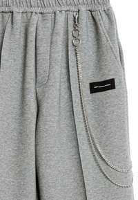 Pantalones de chándal grises hechos de una tela suave, con una cinturilla elástica, bolsillos laterales y una cadena plateada adjunta a los bucles como detalle.